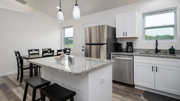 A modern kitchen with a granite countertop, stainless steel appliances, and a dining area with dark chairs. - Beautiful New House on 5 Acres close to springs (High Springs)