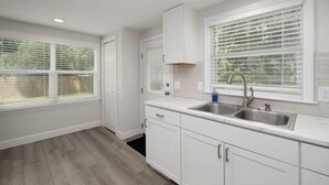 A modern kitchen with white cabinetry, a double sink, and large windows with blinds. - Beautiful New House on 5 Acres close to springs (High Springs)