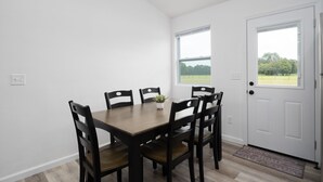 A dining room with a wooden table and six chairs, a small potted plant, and a door with a view of a green landscape. - Beautiful New House on 5 Acres close to springs (High Springs)