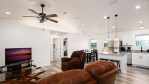 A modern living room with a glass coffee table, leather sofas, a TV, and a ceiling fan. - Beautiful New House on 5 Acres close to springs (High Springs)