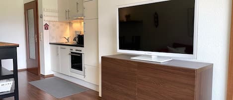 Una cocina moderna con armarios blancos, un horno empotrado y un televisor de pantalla plana grande sobre un mueble de madera.