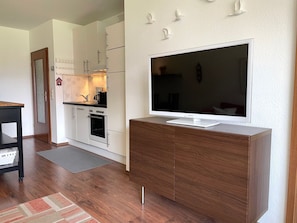 A modern kitchen with white cabinets, a built-in oven, and a large flat-screen TV on a wooden cabinet. - Fewo14 - Haus Land & Meer (Cuxhaven)