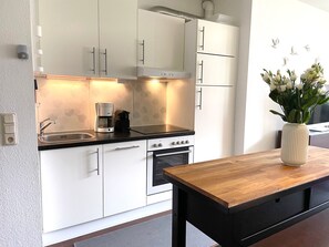 A modern kitchen with white cabinetry, a black countertop, and a wooden table. - Fewo14 - Haus Land & Meer (Cuxhaven)