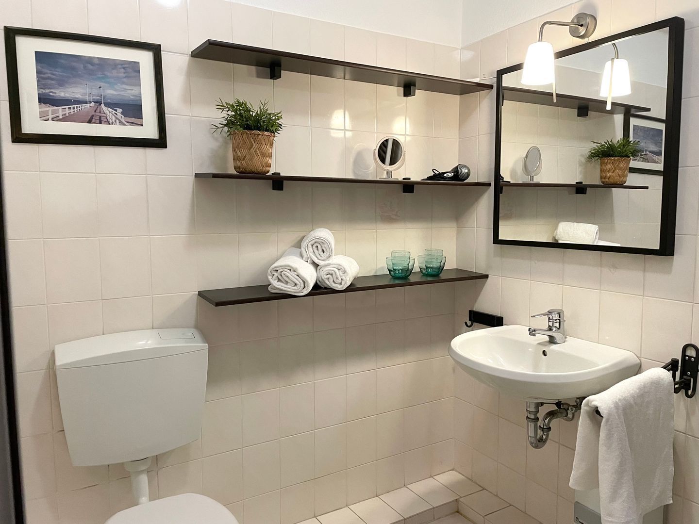 A modern bathroom with a toilet, sink, and shelves with towels and toiletries.