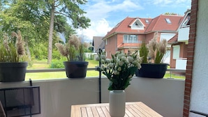 A balcony with a wooden table and chairs, potted plants, and a view of houses. - Fewo14 - Haus Land & Meer (Cuxhaven)