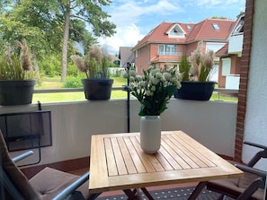 A balcony with a wooden table and chairs, potted plants, and a view of houses. - Fewo14 - Haus Land & Meer (Cuxhaven)