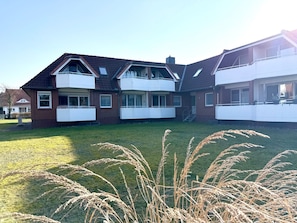 A two-story residential building with a sloped roof, multiple balconies, and a grassy yard. - Fewo14 - Haus Land & Meer (Cuxhaven)