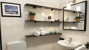 A modern bathroom with a toilet, sink, and shelves with towels and toiletries. - Fewo14 - Haus Land & Meer (Cuxhaven)