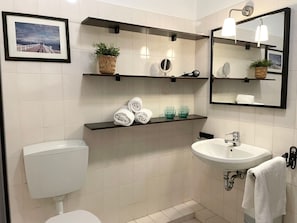 A modern bathroom with a toilet, sink, and shelves with towels and toiletries. - Fewo14 - Haus Land & Meer (Cuxhaven)