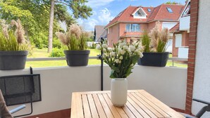 A balcony with a wooden table, potted plants, and a white vase with flowers.