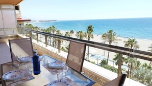 A balcony with a table set for two, overlooking a beach with palm trees and the ocean. - Apartamento 3 Habitaciones Primera Linea de Playa (Estepona)