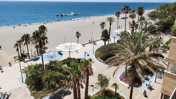 A beach resort with a wide sandy beach, palm trees, and a view of the ocean. - Apartamento 3 Habitaciones Primera Linea de Playa (Estepona)