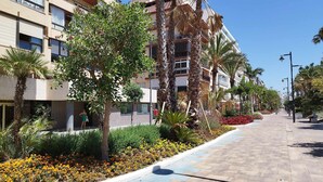 A multi-story hotel with balconies, surrounded by palm trees and a flower-lined pathway. - Apartamento 3 Habitaciones Primera Linea de Playa (Estepona)