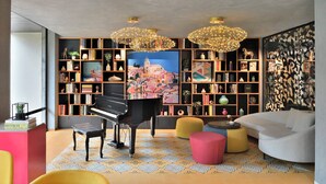 Un salon moderne agrémenté d’un piano à queue, d’un tapis aux motifs colorés et d’une grande bibliothèque remplie de livres et d’objets décoratifs.