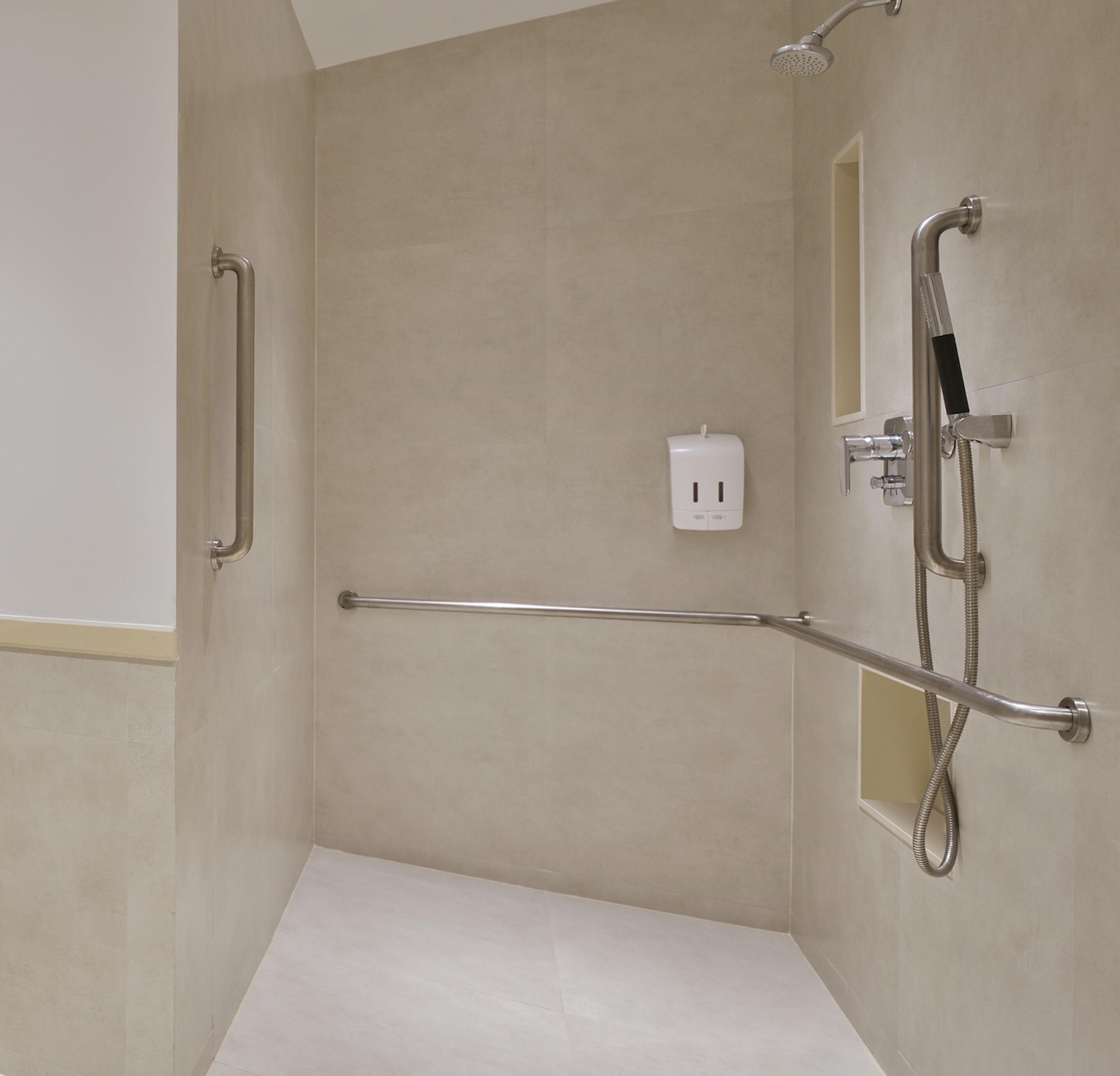 Un baño moderno con cabina de ducha, barras de apoyo y ducha de mano.