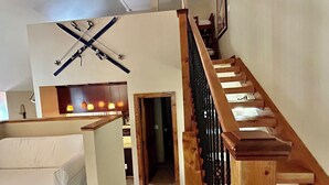 Ein modernes Wohnzimmer mit einer Holztreppe, einem weißen Sofa und einem Skiständer an der Wand.