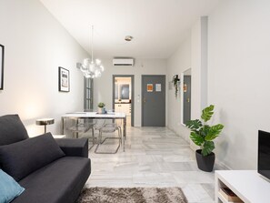 Ein modernes Wohnzimmer mit einem grauen Sofa, einem Esstisch mit Stühlen, einer Topfpflanze und einem TV-Schrank.
