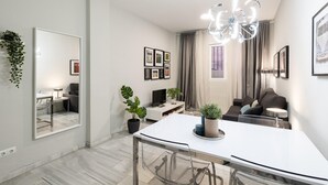 A modern living room with a glass dining table, a sofa, a TV, and a chandelier.