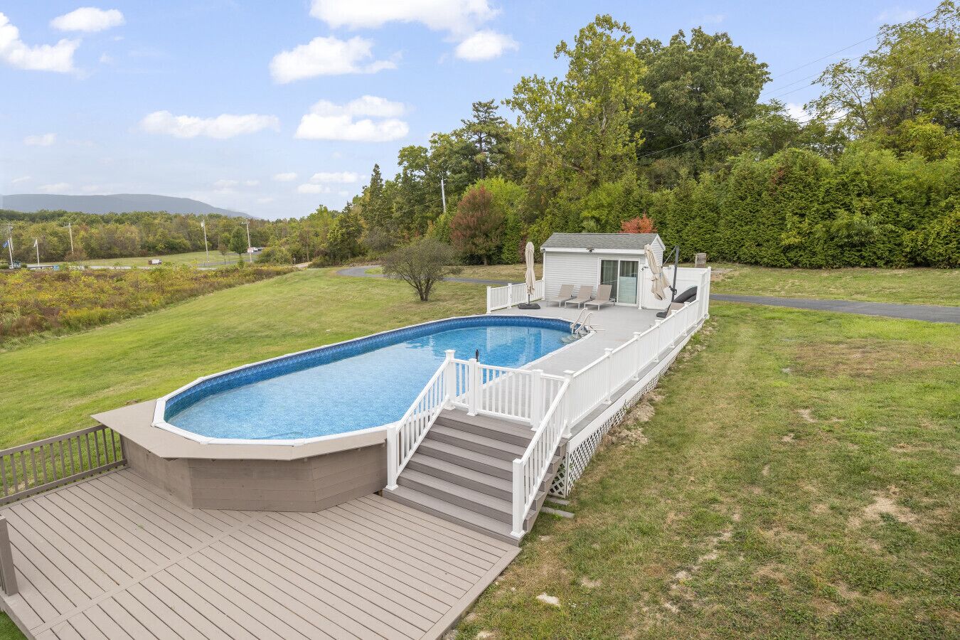 A rectangular swimming pool with a deck and a small covered area with chairs.
