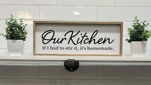 Un letrero enmarcado sobre una pared de azulejos blancos con el texto: 'Nuestra cocina. Si tuviera que removerlo, es casero.'