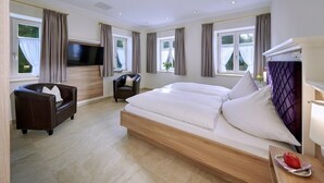 Ett modernt hotellrum med en stor säng, en soffa, en TV och ett matbord med en fruktfat.
