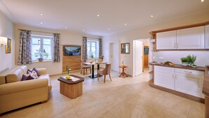 Una sala de estar moderna con sofá, mesa de centro y comedor. Hay un televisor montado en la pared, una cocina con armarios y una puerta que conduce a otra habitación.