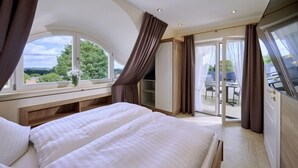 Et soveværelse med en stor seng, et vindue med udsigt over grøn vegetation og en skydedør til en balkon.
