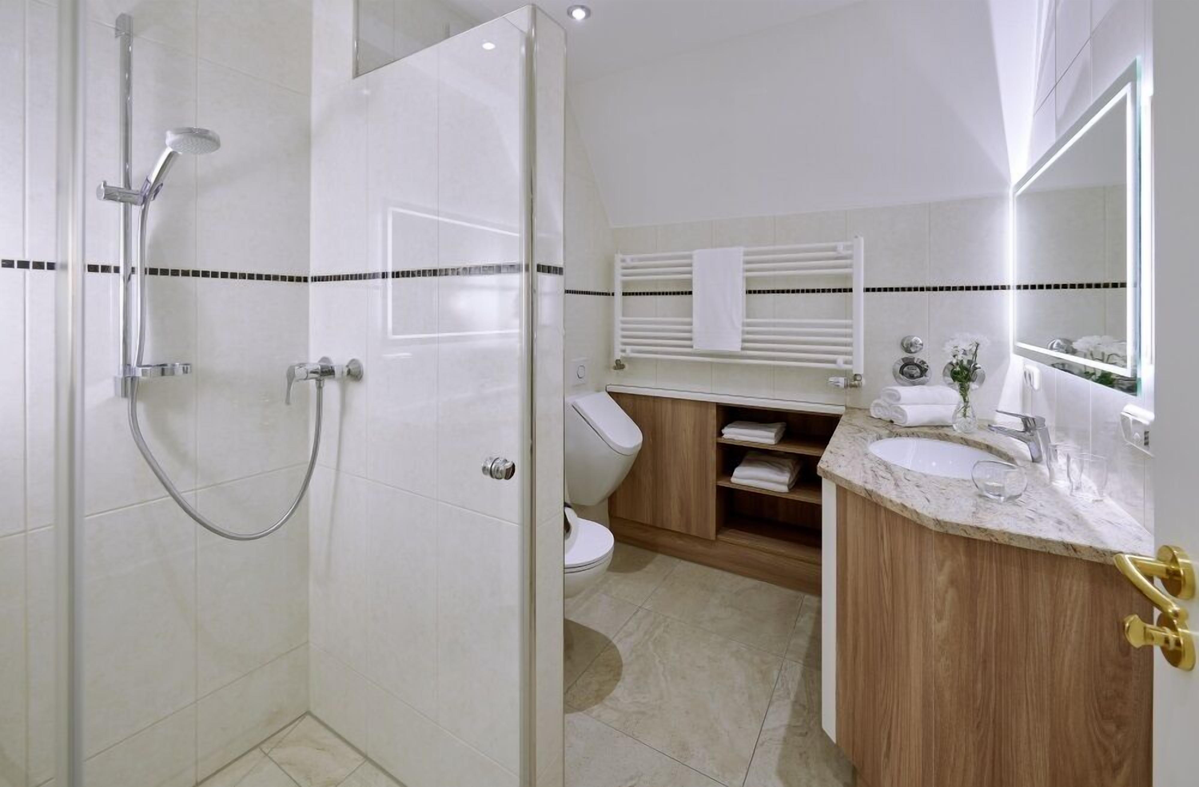 A modern bathroom with a glass-enclosed shower, a wooden vanity with a sink, and a mirror with integrated lighting.