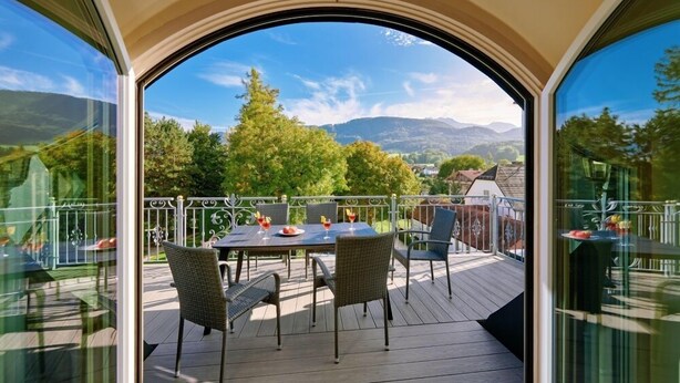 A balcony with a table and chairs, overlooking a scenic landscape with trees and mountains. - Ferienwohnung 10 für 1-5 Personen (Bernau am Chiemsee)