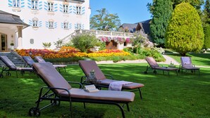 A hotel with outdoor sun loungers, a well-maintained garden, and a building with distinctive blue window shutters.