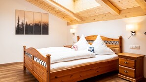 A wooden bed with a slatted headboard, a bedside table, and a nightstand. There is a skylight above the bed, and wall-mounted lights are visible. - Ferienwohnung Jennerblick, 85 qm, 1-4 Personen, 2 Separate Schlafzimmer, Wohn- Esszimmer, Bad, Balkon (Schönau am Königssee)