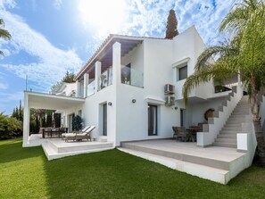 Ein modernes, zweistöckiges Haus mit einer überdachten Terrasse, Sitzgelegenheiten im Freien und einer Treppe, die zum oberen Stockwerk führt.