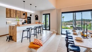 A modern kitchen with wooden accents, a bar area, and a dining space with a view. - Top Renovated 4BDRM Luxury Villa - Frontline Golf (Benahavís)