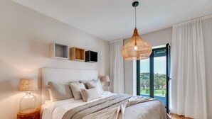 A bedroom with a large bed, a hanging light fixture, a view of the outdoors through a window, and a wooden floor. - Top Renovated 4BDRM Luxury Villa - Frontline Golf (Benahavís)