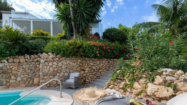 A pool area with a stone wall, a lounge chair, and a dining setup with fruits and vegetables. - Top Renovated 4BDRM Luxury Villa - Frontline Golf (Benahavís)
