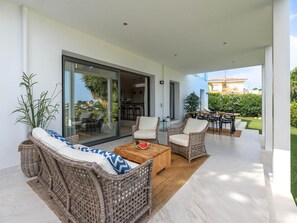 Ein moderner Außenbereich mit Korbmöbeln, einem Holztisch und Blick auf den Garten sowie das Haus im Hintergrund.