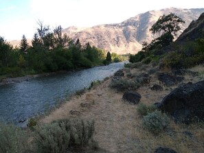 Un río con un sendero rocoso y abundante vegetación, con montañas al fondo.
