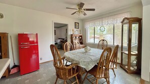 A dining area with a red refrigerator, wooden chairs, a table with a lace tablecloth, and a ceiling fan.