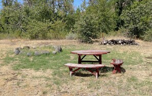 Una mesa de picnic con bancos en un campo cubierto de césped y árboles al fondo.