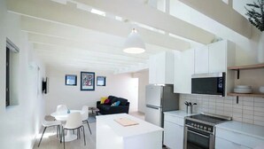 A modern kitchen with white cabinetry, a built-in oven, and a microwave. There is a dining area with a white table and chairs. - Downtown Bend Vacation Cottage (Bend)