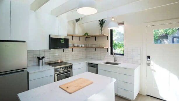 A modern kitchen with white cabinetry, a built-in oven, a microwave, and a large island with a cutting board. - Downtown Bend Vacation Cottage (Bend)