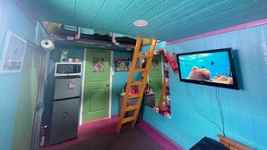 A room with teal walls, a green door, a wooden ladder, a microwave, a refrigerator, and a TV displaying an underwater scene.