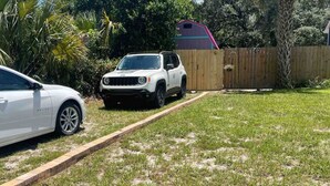 A white SUV parked in a grassy yard with a wooden fence and a shed in the background.