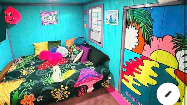 A room with teal walls, a colorful bedspread, and a door with a vibrant mural.