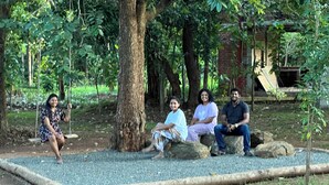 Un grupo de personas sentadas en un banco de piedra en un parque, con árboles y un edificio de ladrillo al fondo.