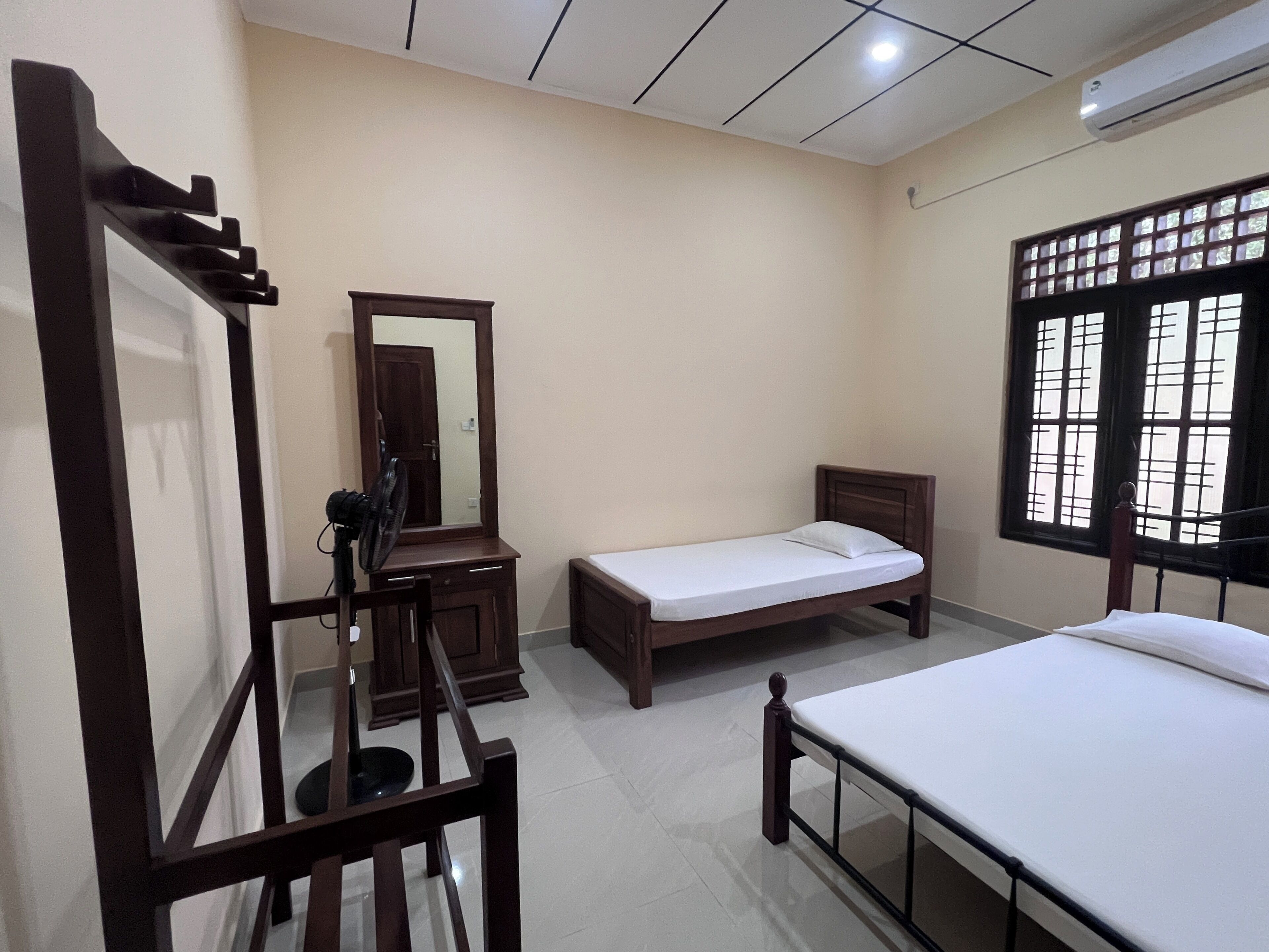 Un dormitorio con cama, mesita de noche, espejo, cómoda y ventana con barrotes.