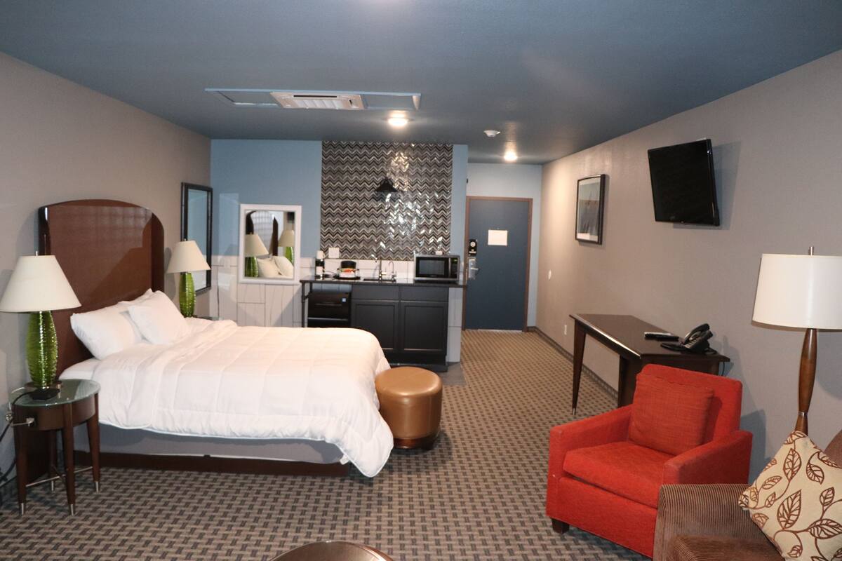 A hotel room with a bed, a red armchair, a small table, a lamp, a microwave, and a kitchenette.