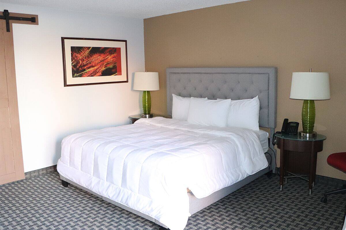 A hotel room with a large bed, two bedside tables with lamps, a framed picture on the wall, and a red chair.