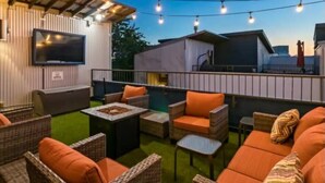 Un área de patio al aire libre con mobiliario de mimbre, un televisor de pantalla plana y luces colgantes.