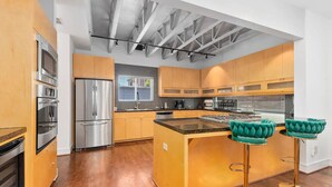 Una cocina moderna con electrodomésticos de acero inoxidable, armarios de madera y una isla central con taburetes de bar.